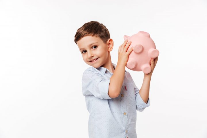 Portrait of a happy cute little kid holding piggy bank and looking at camera isolated over white background